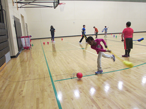 Abi Jepsen swings a hockey stick at a ball that is tethered to the bleachers.